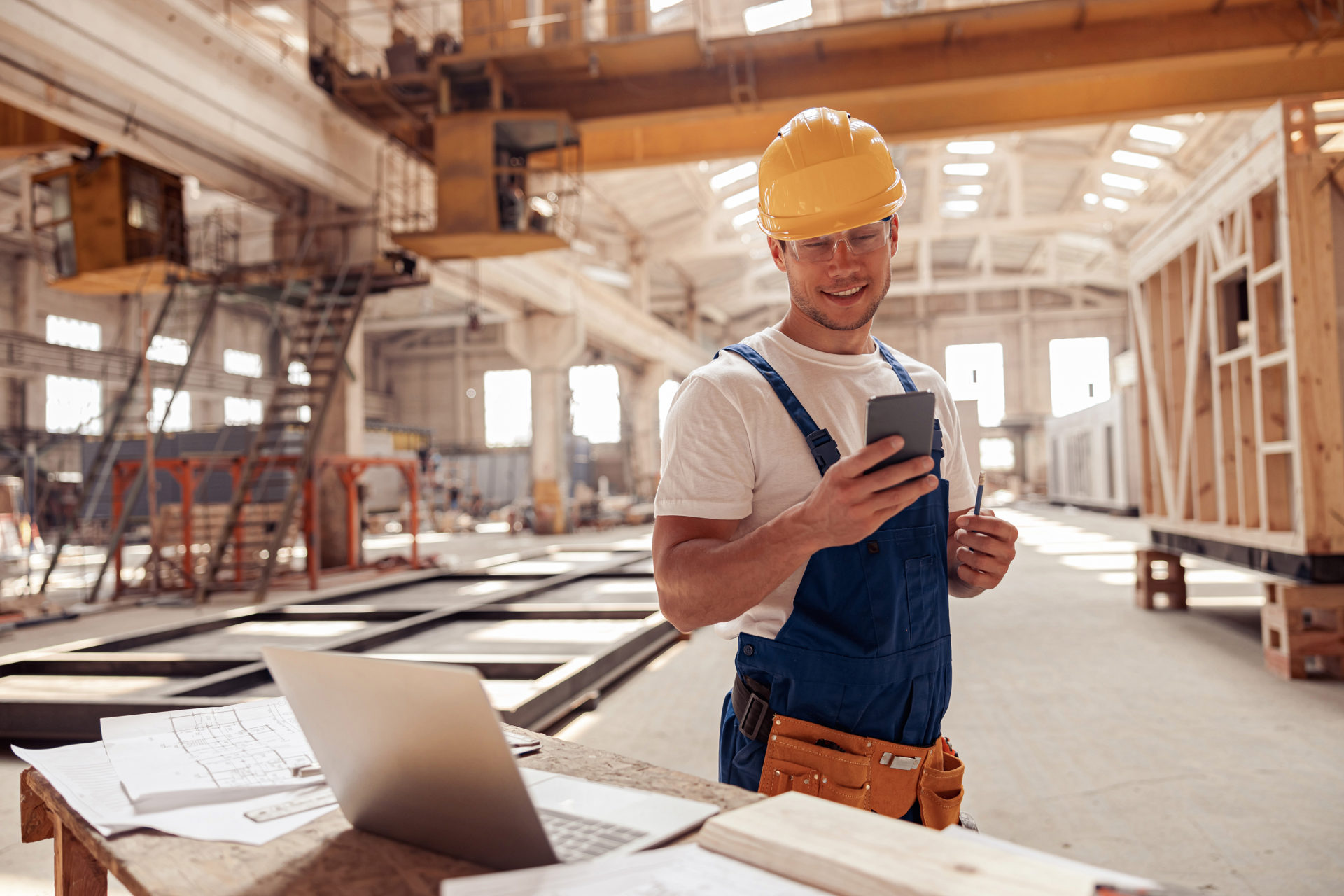Glücklicher Bauarbeiter schaut auf Baustelle auf sein Handy